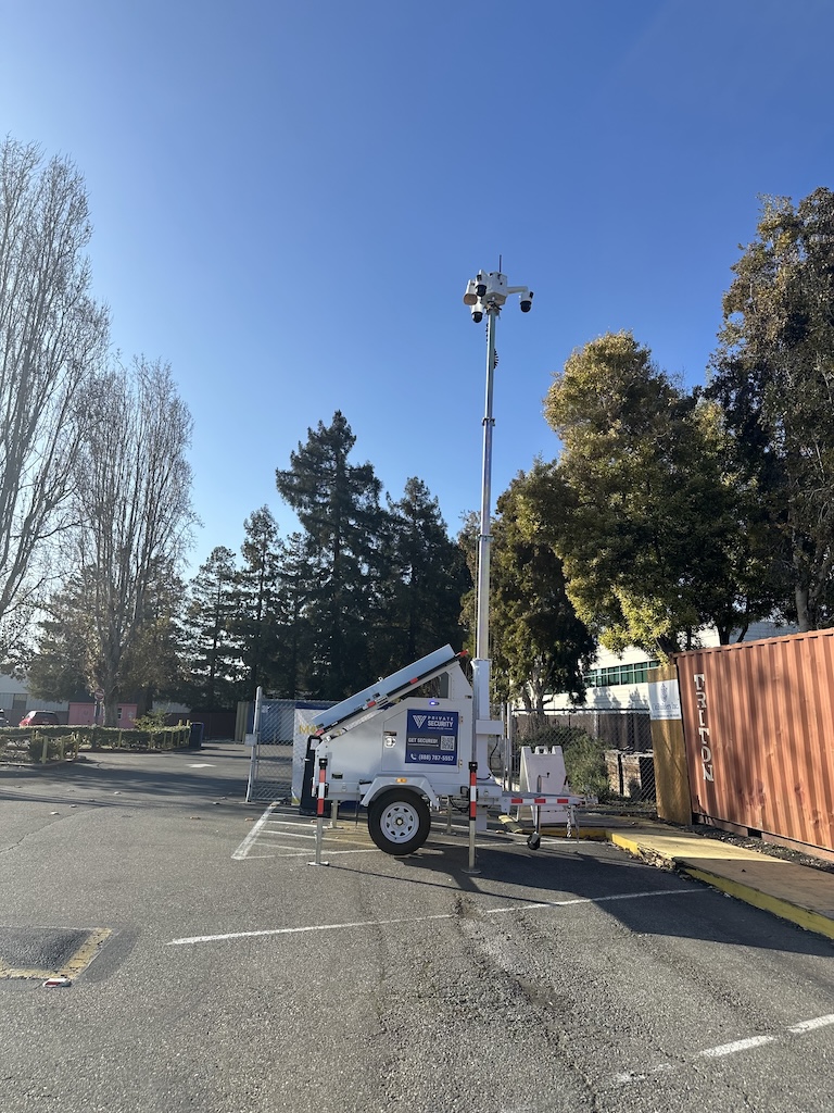 A mobile surveillance tower with three mounted security cameras in a parking lot, deployed by Private Security Plus, under a clear blue sky.